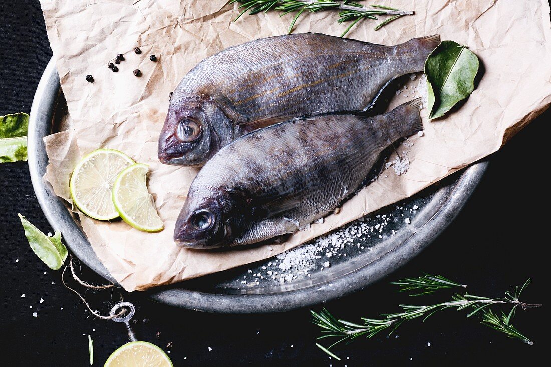 Two seabream fish with rosemary, lime and sea salt server on baking paper