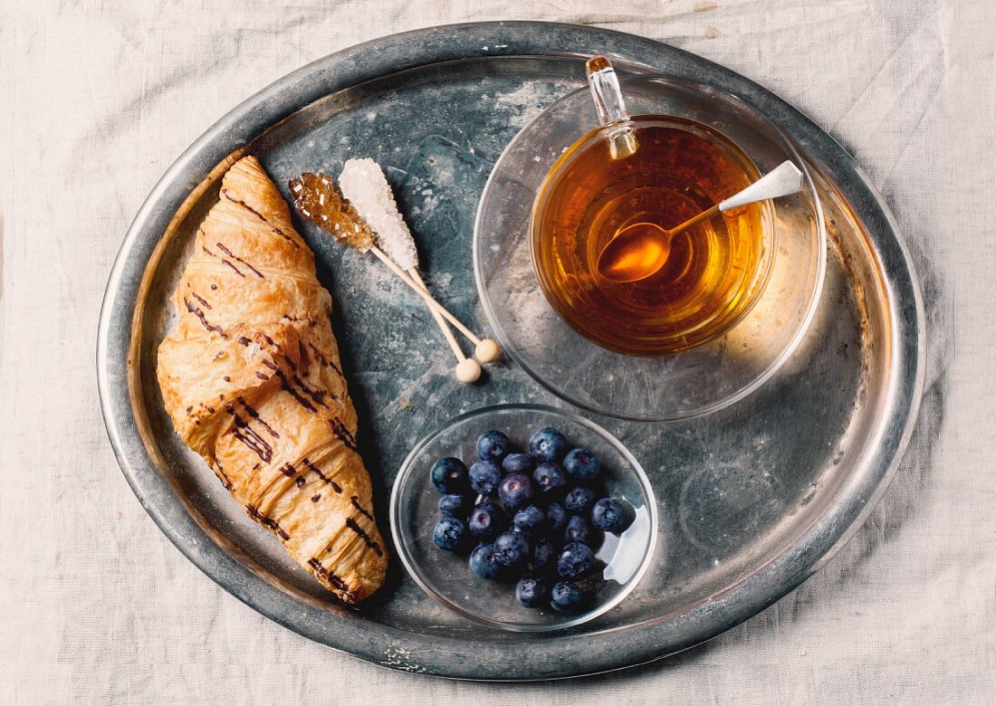A cup of tea, croissants and blueberries on an old-fashioned tray