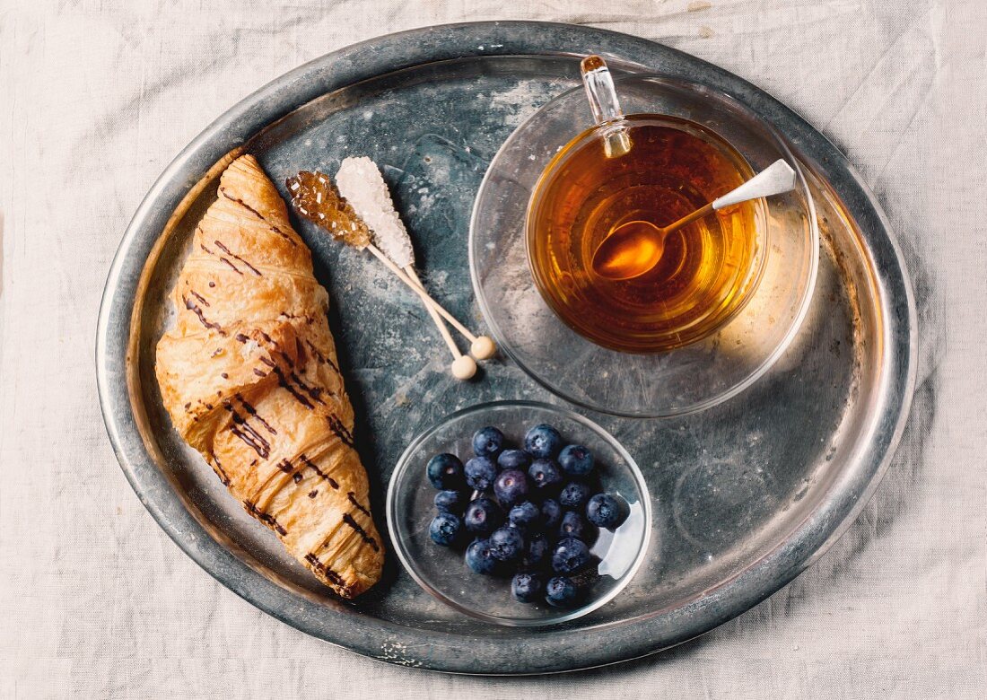 Vintage-Tablett mit Teetasse, Croissants und Blaubeeren