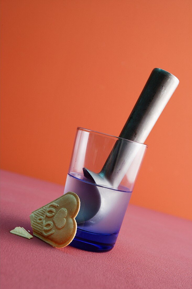 An ice cream scoop in a glass of water with a wafer