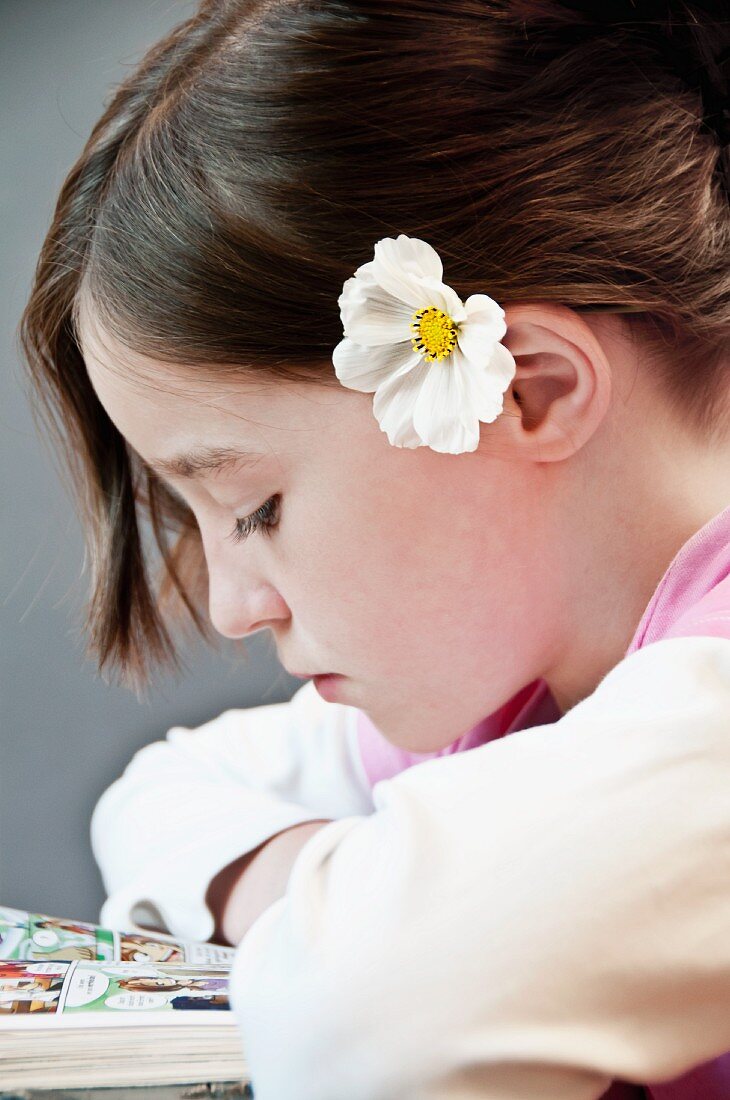 Mädchen mit weisser Cosmeablüte im Haar beim Lesen