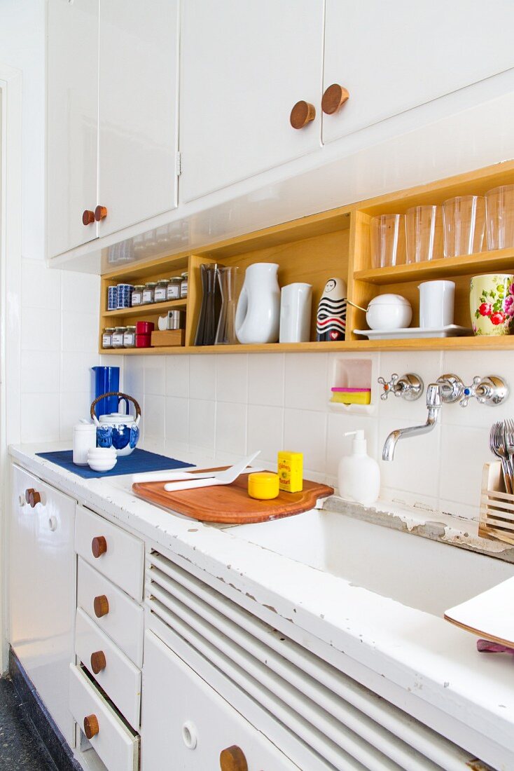 60s-style kitchen with white-painted base and wall units, wooden handles, white-painted worksurface and wooden crockery shelf on wall
