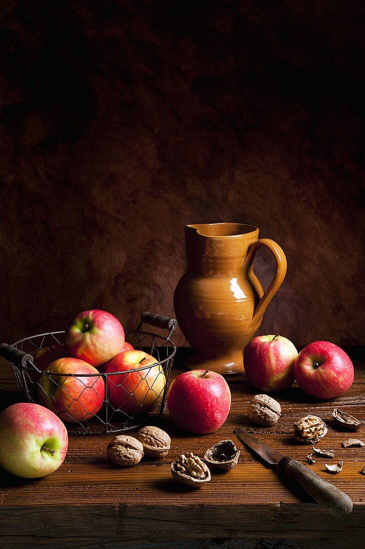 An arrangement featuring apples, walnuts, an earthenware jug and a knife
