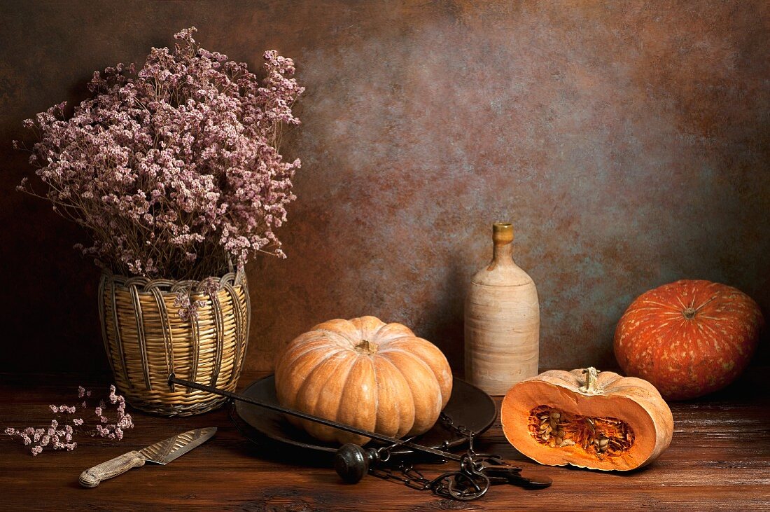 An arrangement featuring pumpkins, dried flowers, an old pair of scales, a bottle and a knife