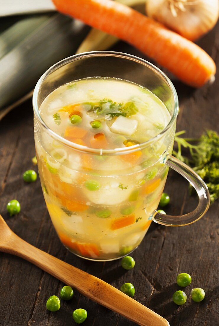 A glass of vegetable stock with carrots and peas