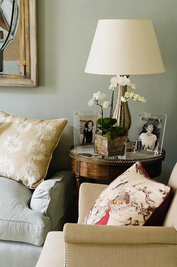 Photos, orchid and lamp with lamps shade on side table between two armchairs