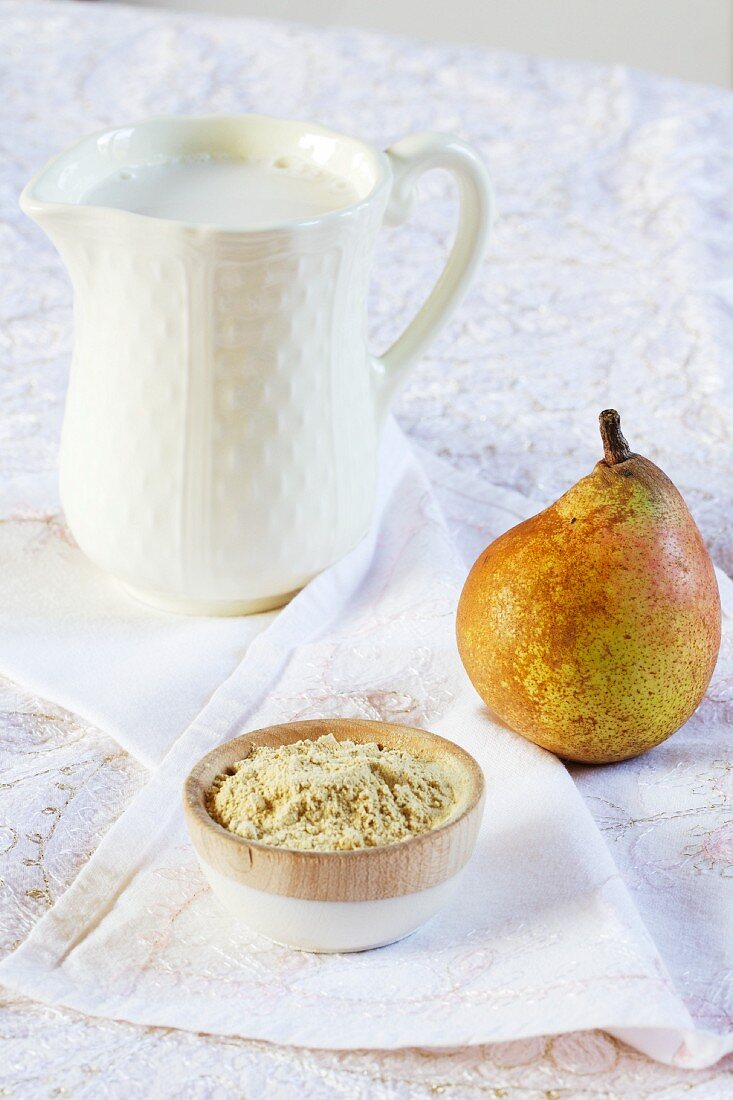 A bowl of carob bean gum, a pear and a jug of rice milk