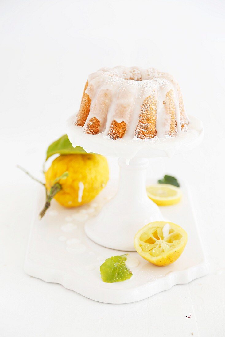 Lemon Bundt cake with light icing on a white cake stand