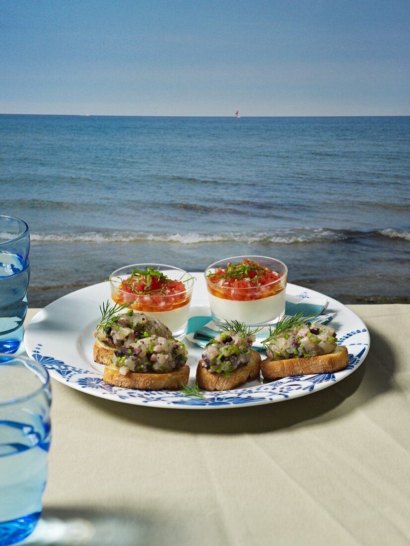 Buttermilk mousse and slices of bread topped with soused herring tartar on a table overlooking the sea