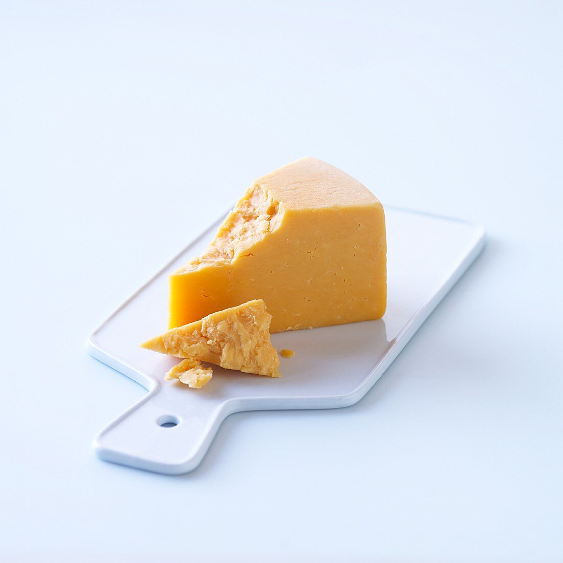 A slice of hard cheese on a plastic board