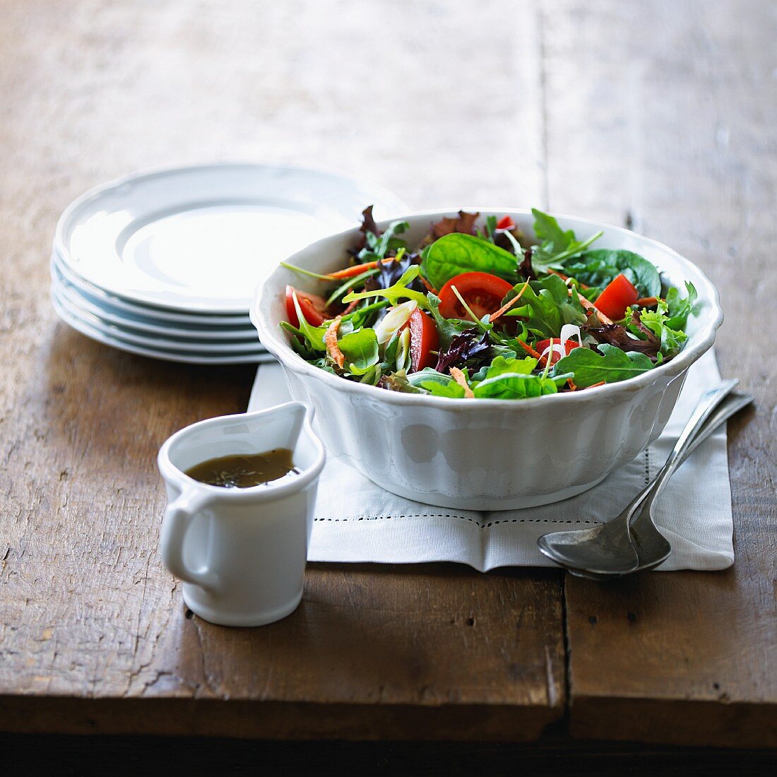 Green salad with tomatoes and a jug of vinaigrette