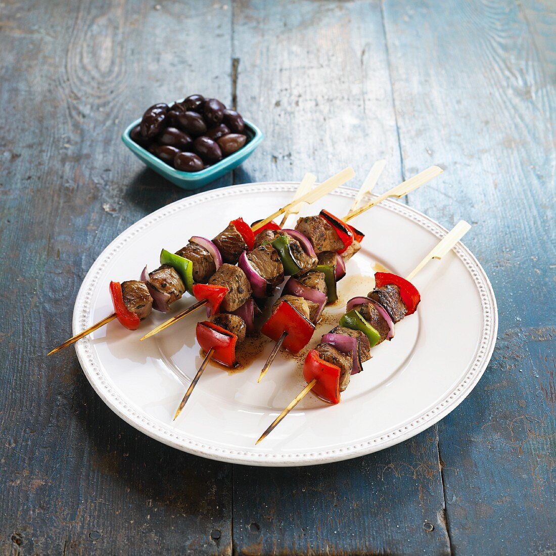Lamb kebabs with pepper and onions served with a bowl of olives