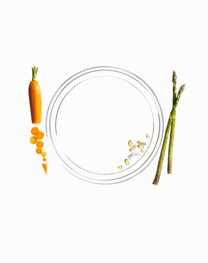 Pills on a plate with a carrot and green asparagus next to it