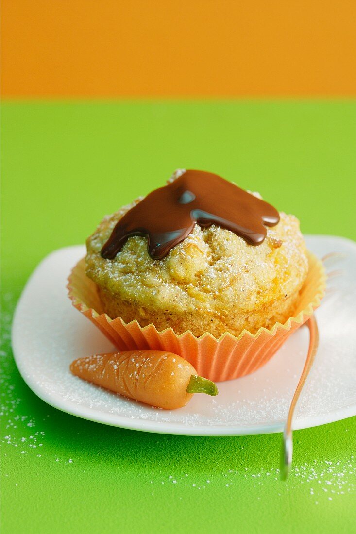 A carrot muffin topped with chocolate glaze next to a marzipan carrot