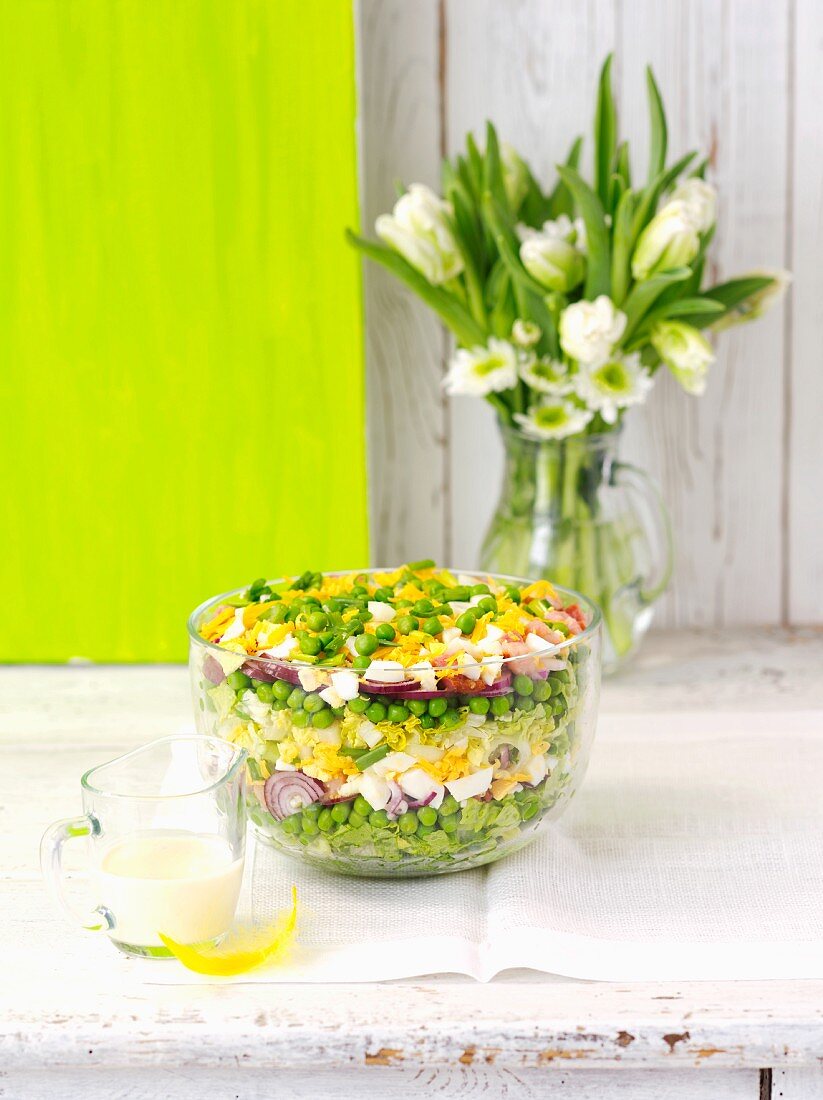 A layered salad with peas, red onions, egg, smoked bacon, lettuce and cheddar cheese