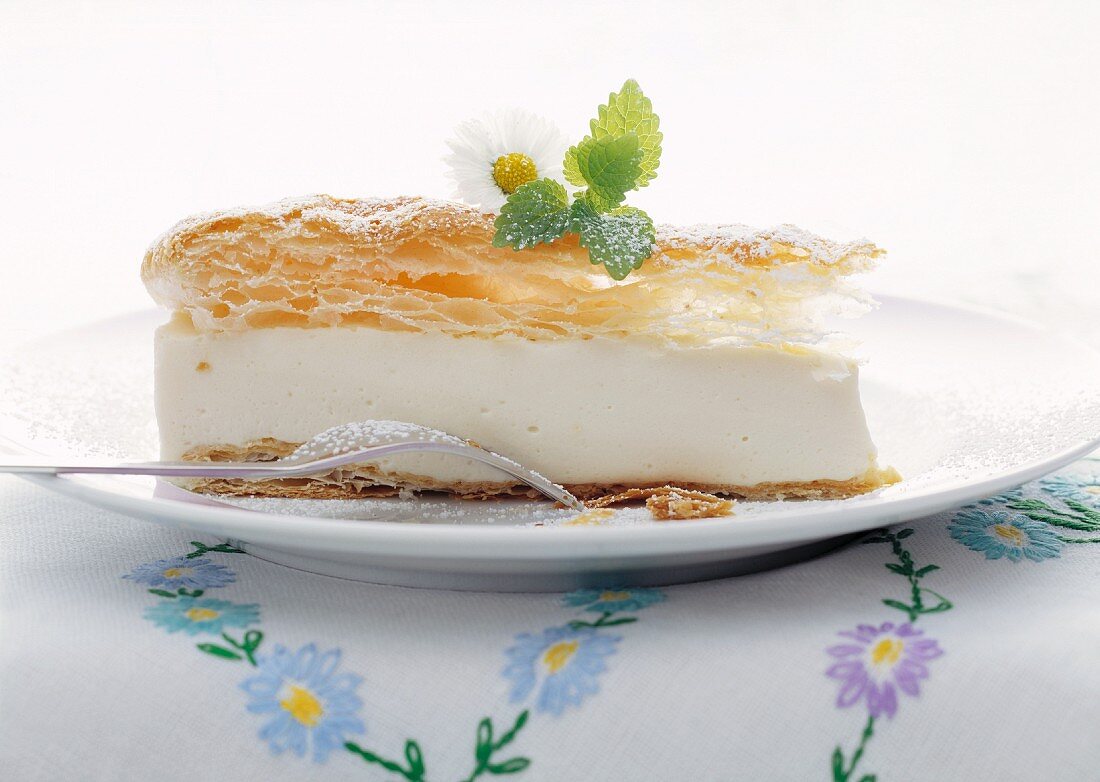 Slice of cheese cake topped with puff pastry and garnished with a sprig of mint and Daisy