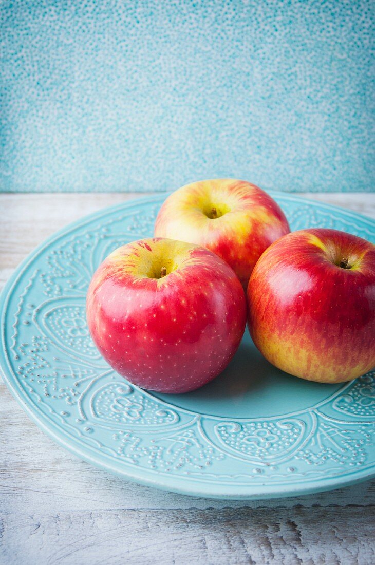 Three Pink Lady apples on a blue ceramic plate