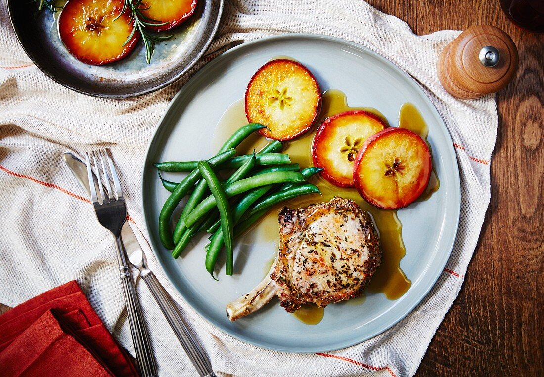 A pork chop with rosemary, apples, maple syrup and green beans
