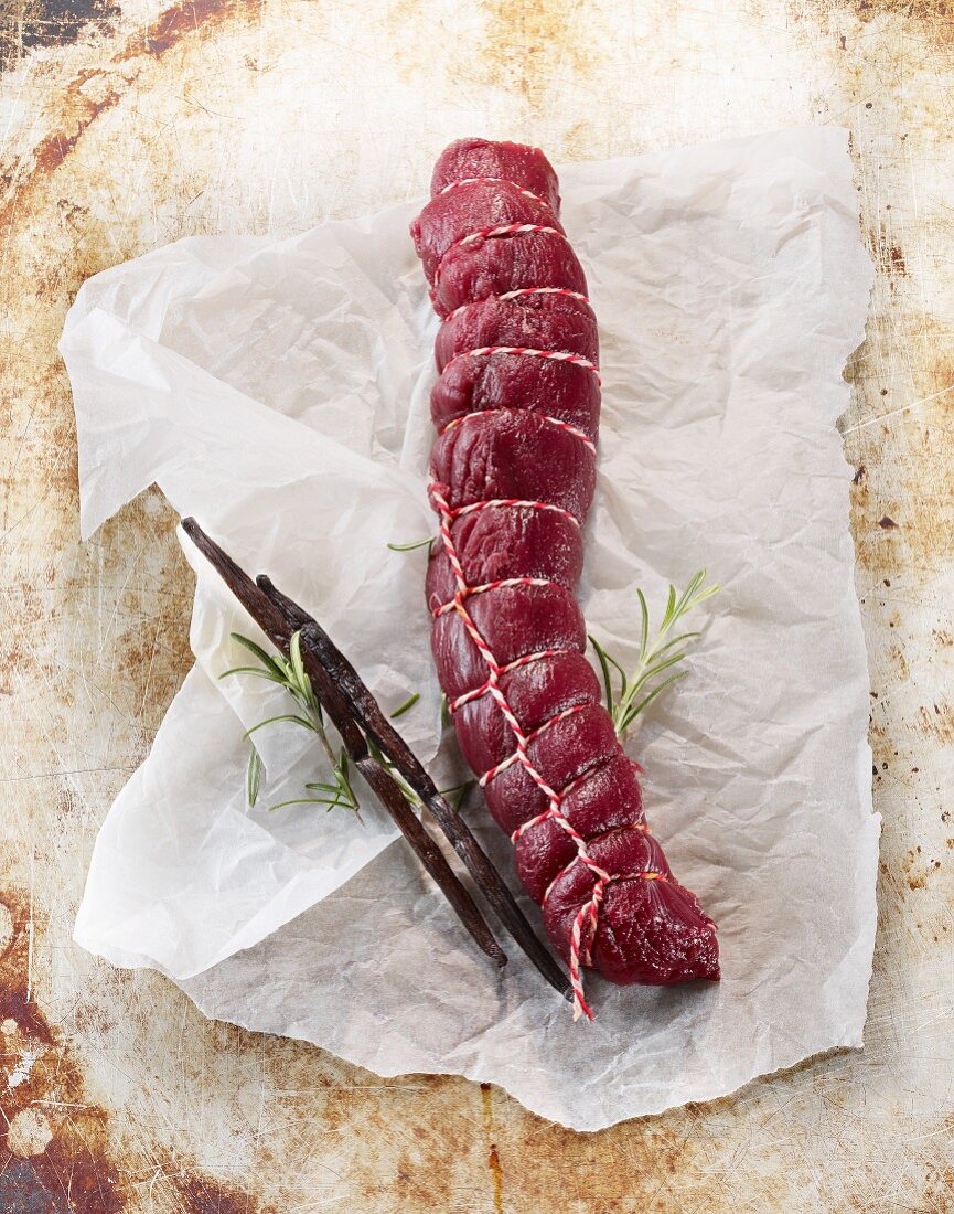 Raw saddle of venison with rosemary and vanilla pods on a piece of paper