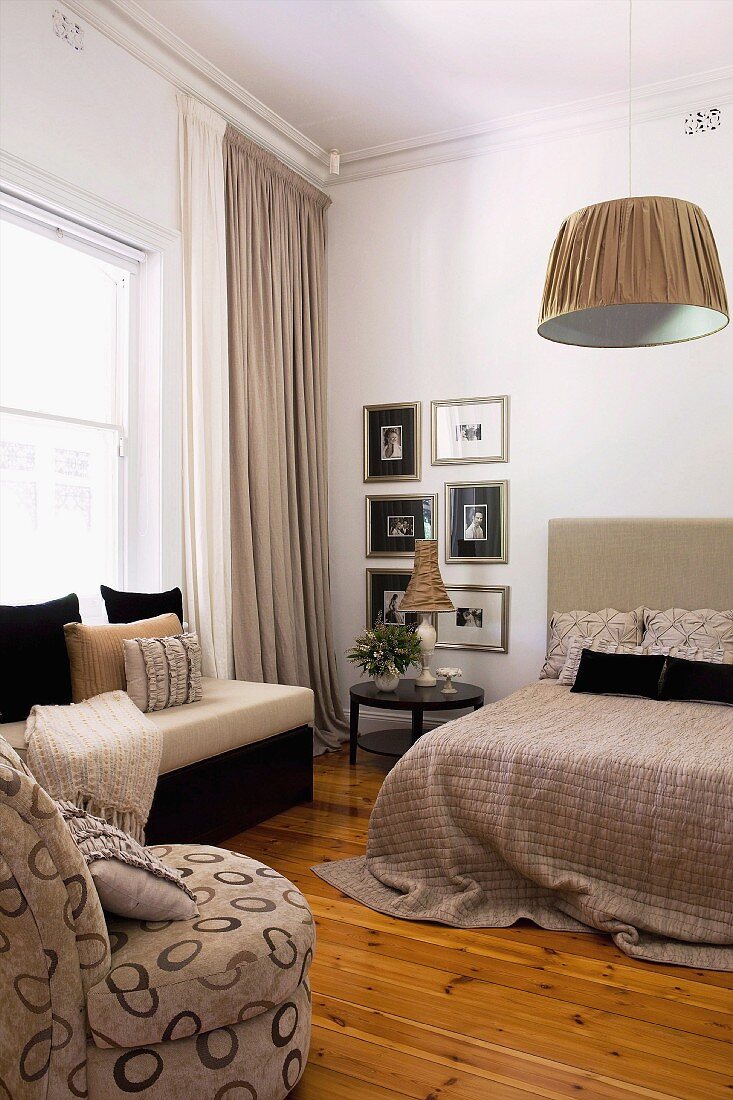 Minimalist bedroom in beige and black with various seating and gallery of pictures next to bed