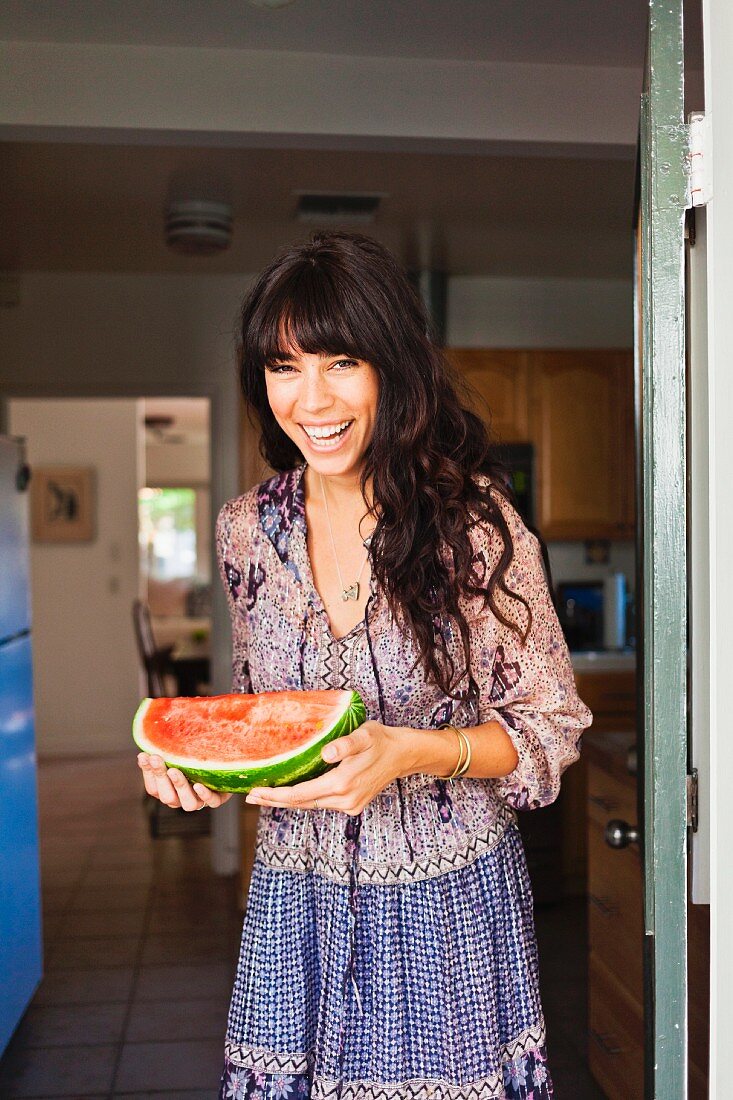 Ayoung woman in a doorway holding a watermelon