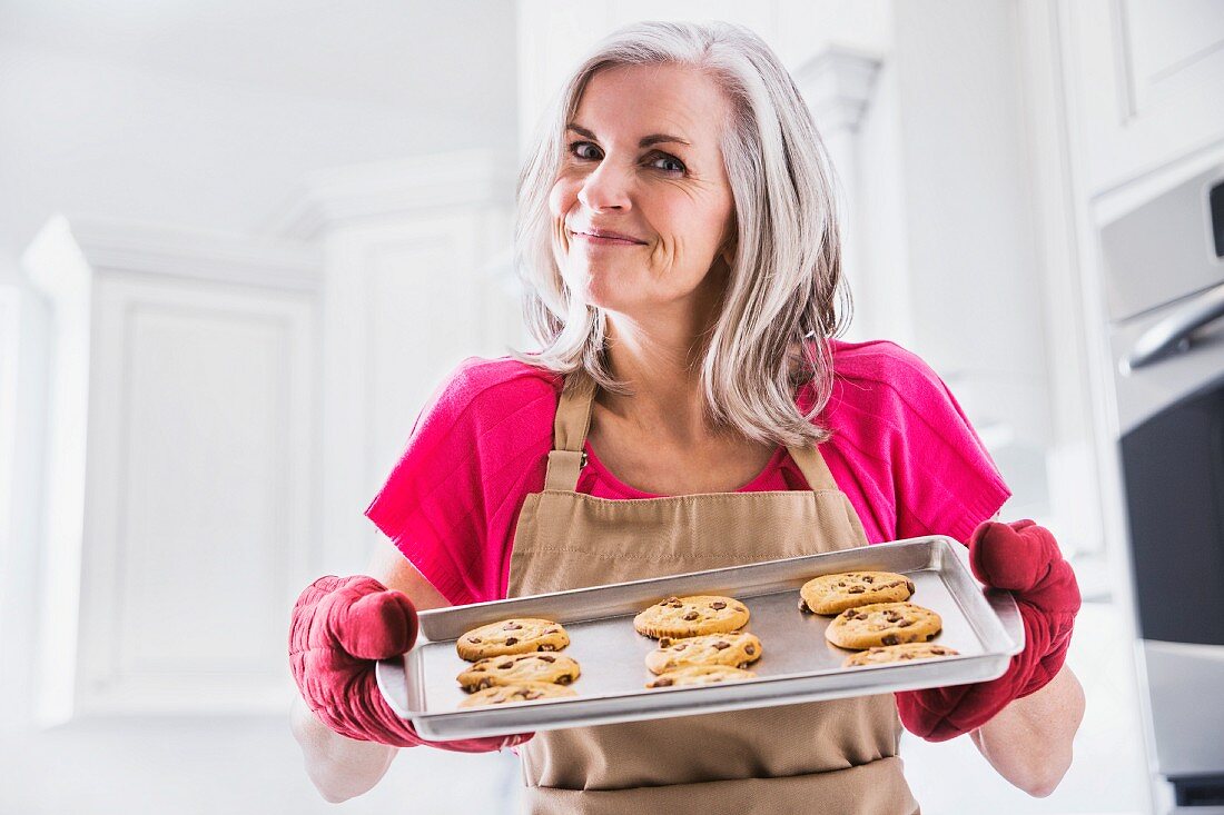 A woman holding a tray of freshly baked chocolate chip cookies