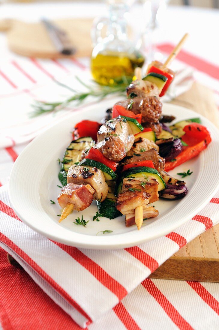 Barbecued kebabs with sausage, bacon and pancetta on grilled vegetables