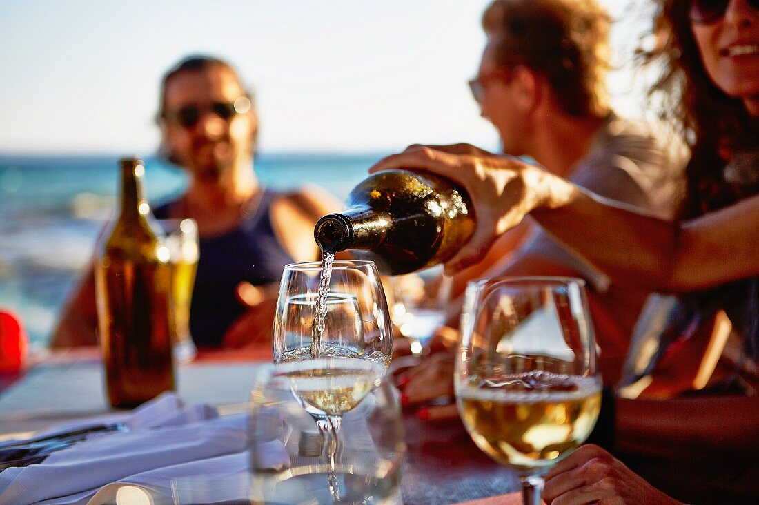 Young people drinking wine at a table in a restaurant overlooking the sea