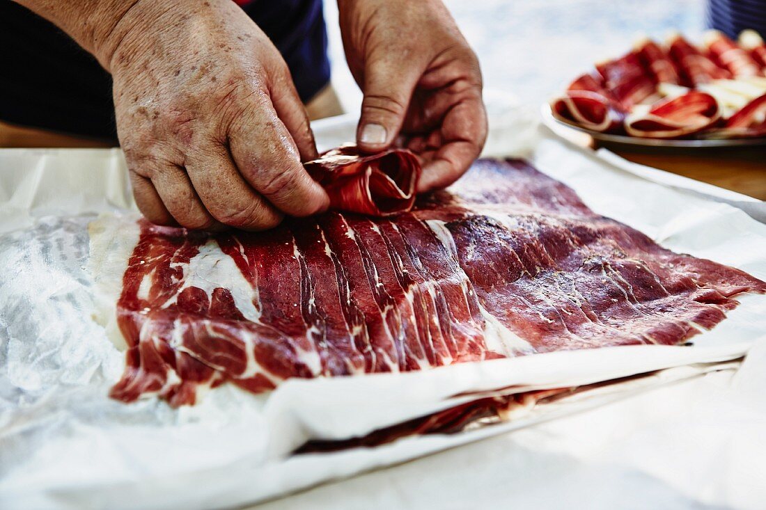 A man rolling slices of serrano ham