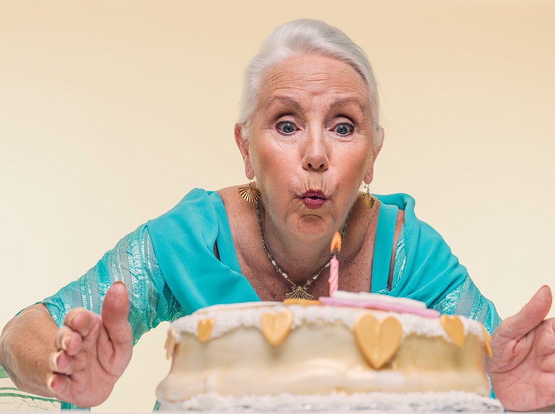 An old lady blowing out candles on a birthday cake