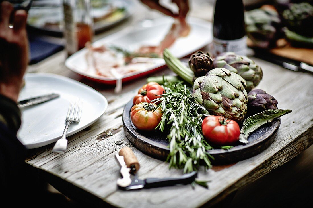 Artichokes, rosemary and tomatoes on a wooden board
