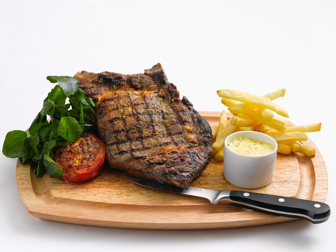 Grilled beef steak with chips, herb butter and tomatoes