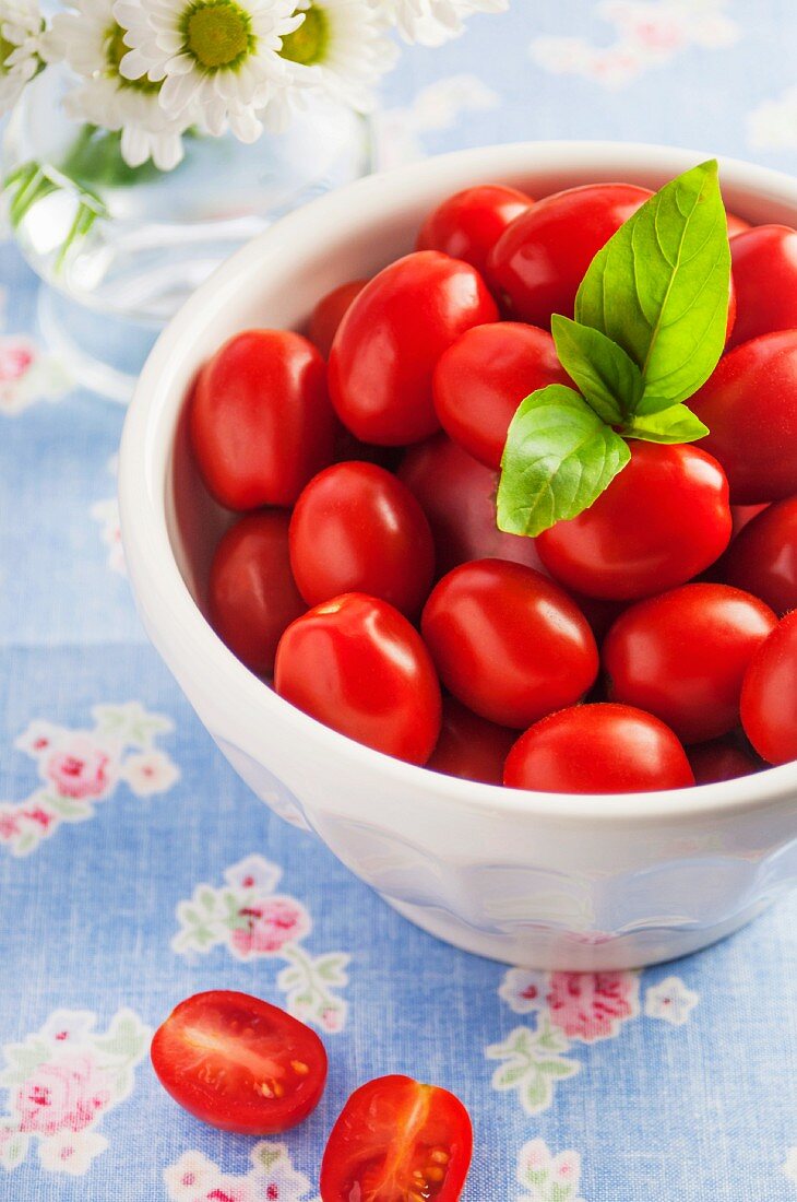 A bowl of fresh organic grape tomatoes with a sprig of basil