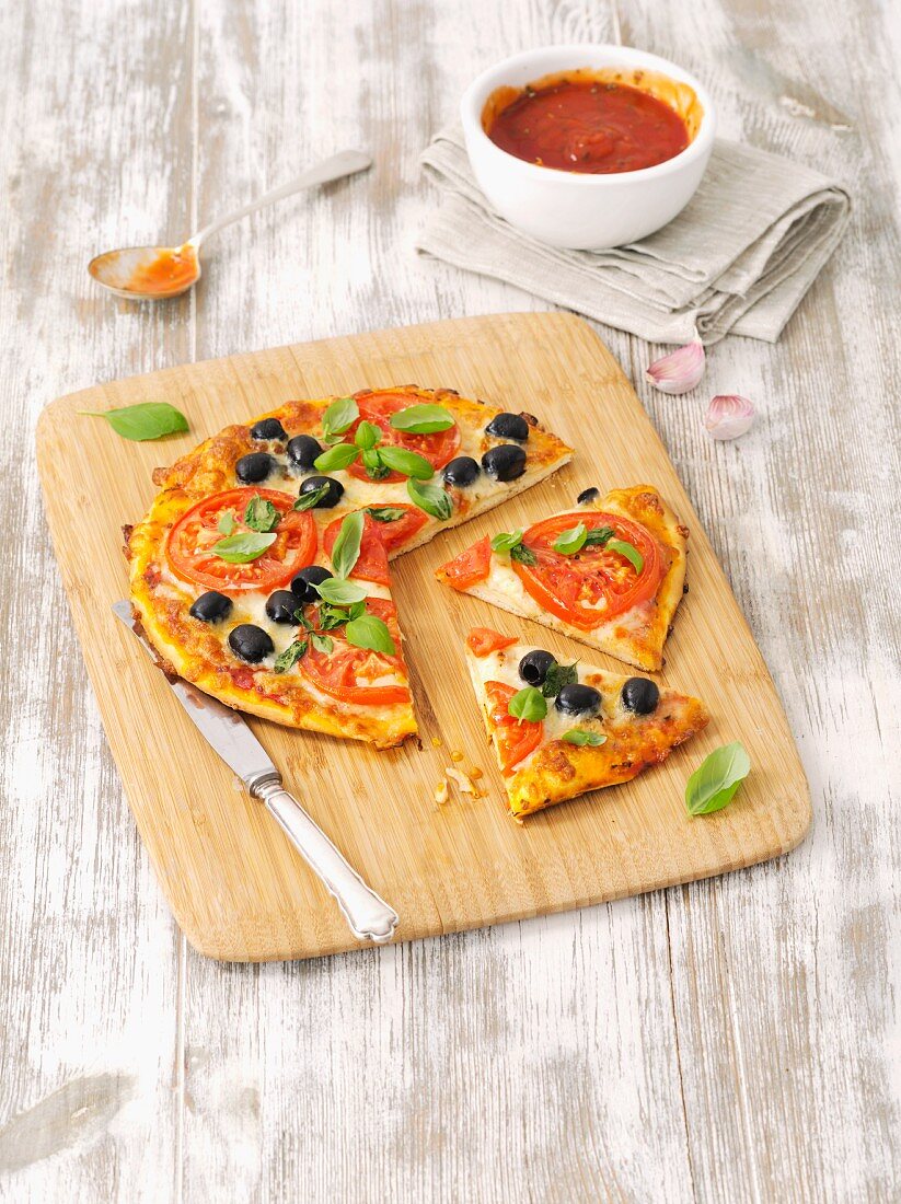 Hausgemachte Pizza mit Tomaten, schwarzen Oliven und Basilikum
