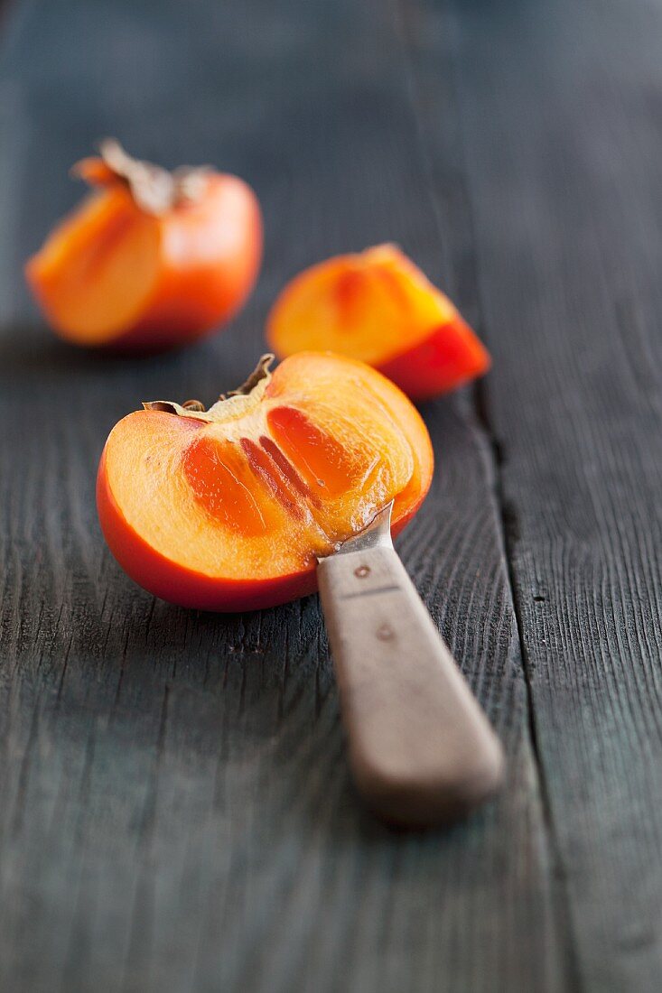 A persimmon, sliced, on a wooden surface