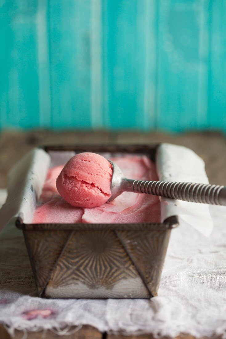 Cranberry sorbet in an ice cream container with an ice cream scoop