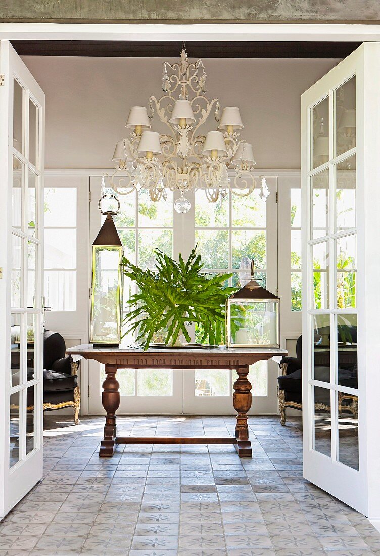 View though open double doors of lanterns on antique table below traditional chandelier with small, white lampshades