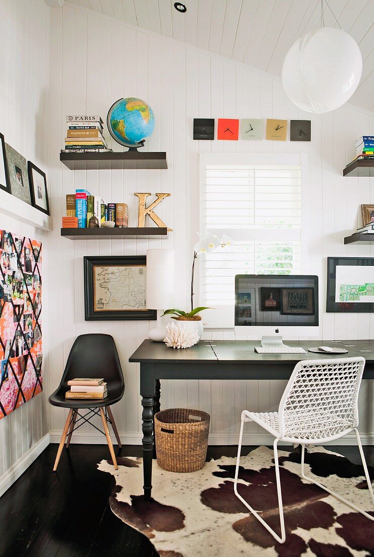 Office area with dark wooden table, metal chair, shell chair, floating shelves & cowhide rug