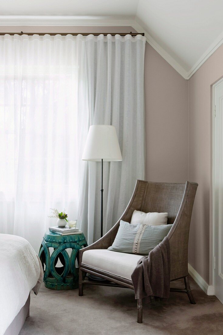 Armchair, side table and standard lamp in front of closed curtains in elegant bedroom