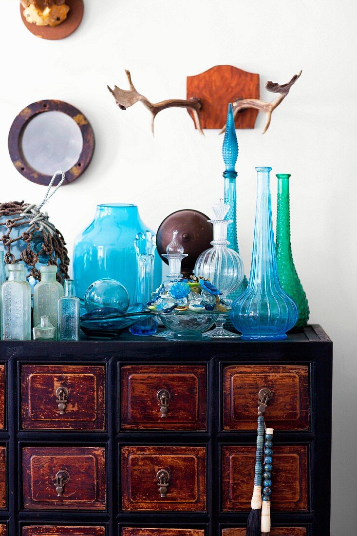 Antlers on wall above colourful glassware on vintage apothecary's cabinet