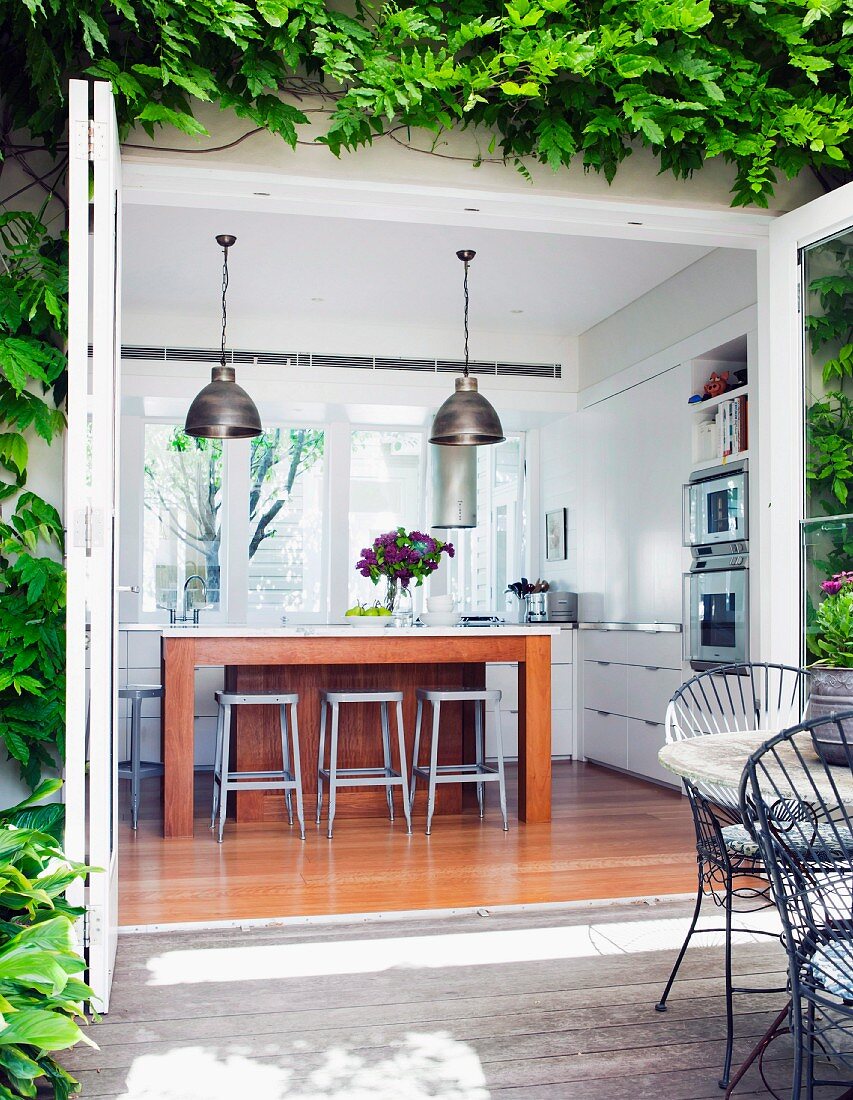 View from terrace through open, folding terrace doors into kitchen with central island and bar stools