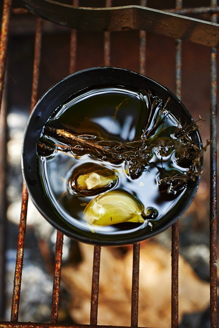 Grillöl mit Kräutern und Knoblauch im Schälchen auf dem Grillrost