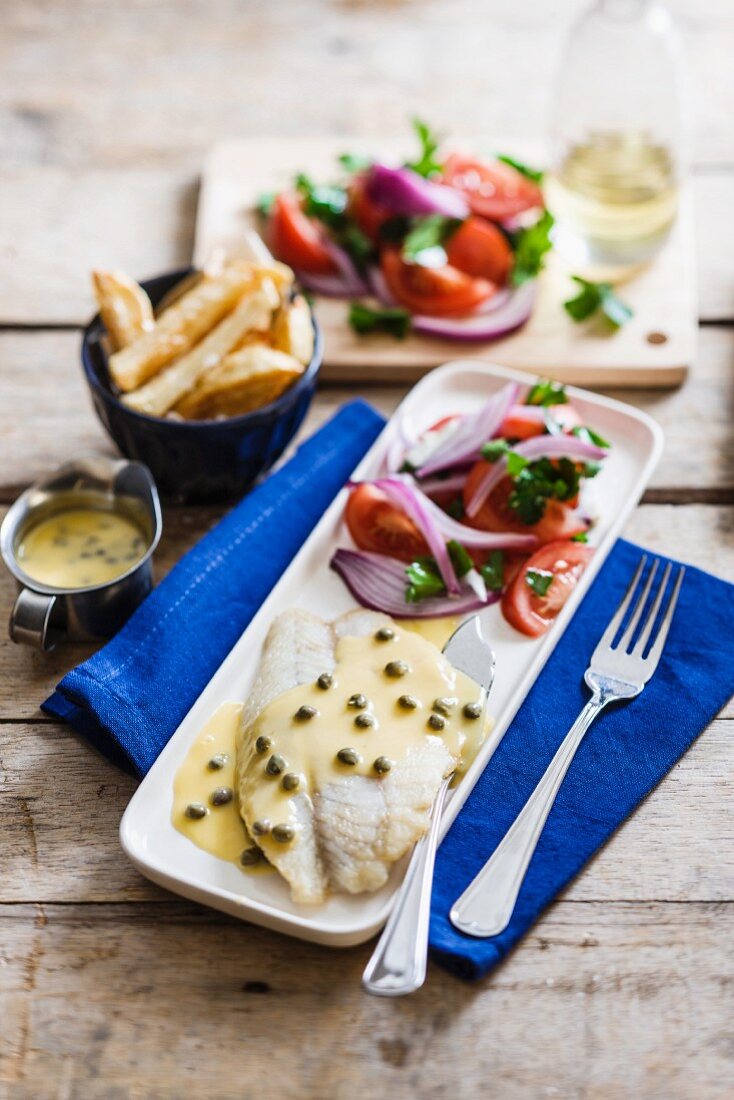 Fish fillet in a lemon and caper sauce with tomato salad and chips