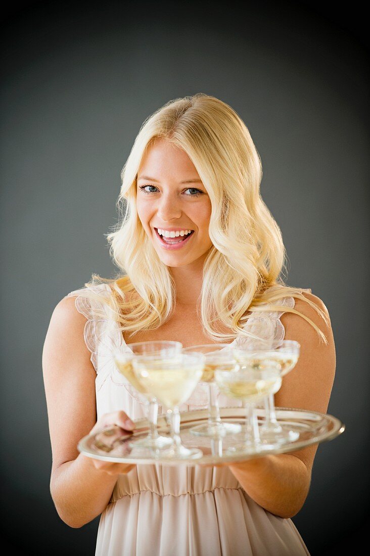 A woman holding a tray of champagne glasses