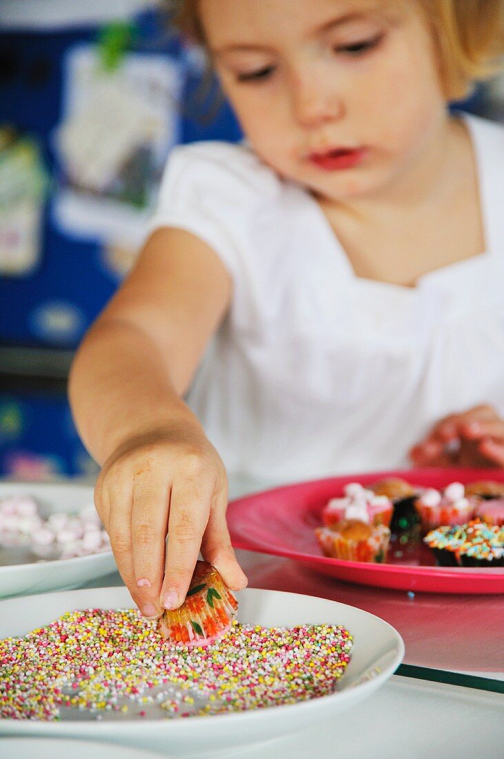 Kleines Mädchen verziert Minimuffins mit Zuckerperlen