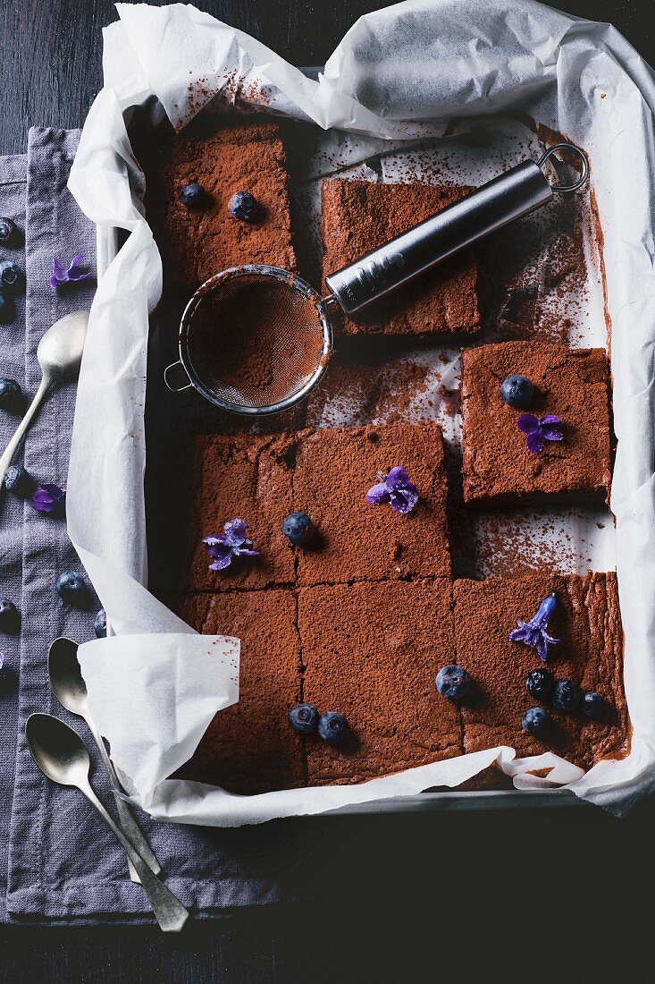 Sliced chocolate cake in a baking tray with blueberries and sugared violets