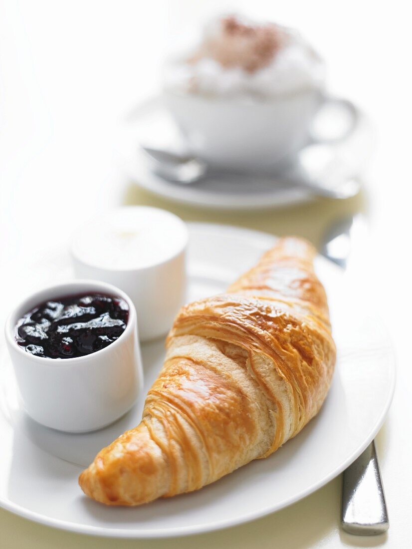 A fresh croissant with blueberry jam and butter