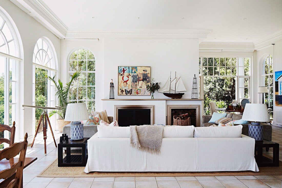 White sofa in front of open fireplace in elegant, traditional living room with arched French windows