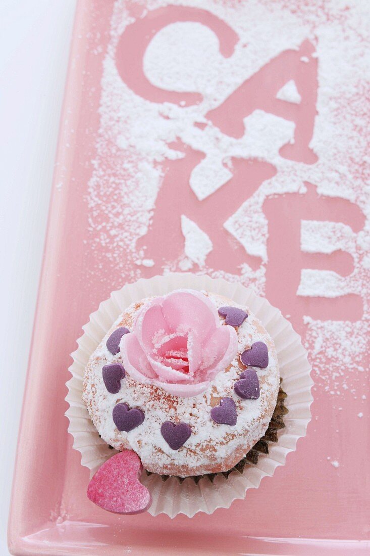 A cupcake decorated with a sugar rose and a hearts for Valentine's Day