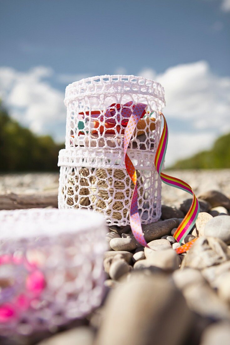 Haberdashery supplies in two, stacked, white crocheted containers on pebbly river bank